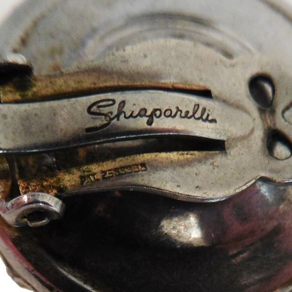 Elsa Schiaparelli, Orecchini, anni ‘60. Orecchini a bottone in metallo dorato e strass iridescenti, sul retro è incisa la sua firma