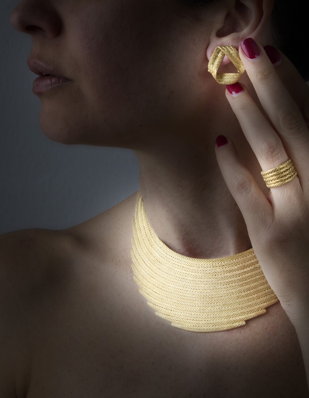 Demi parure Gian Maria Buccellati in oro giallo cesellato con motivo a trecce, composta da collier piatto rastremato alle estremità, orecchini a nastro e anello a fascia