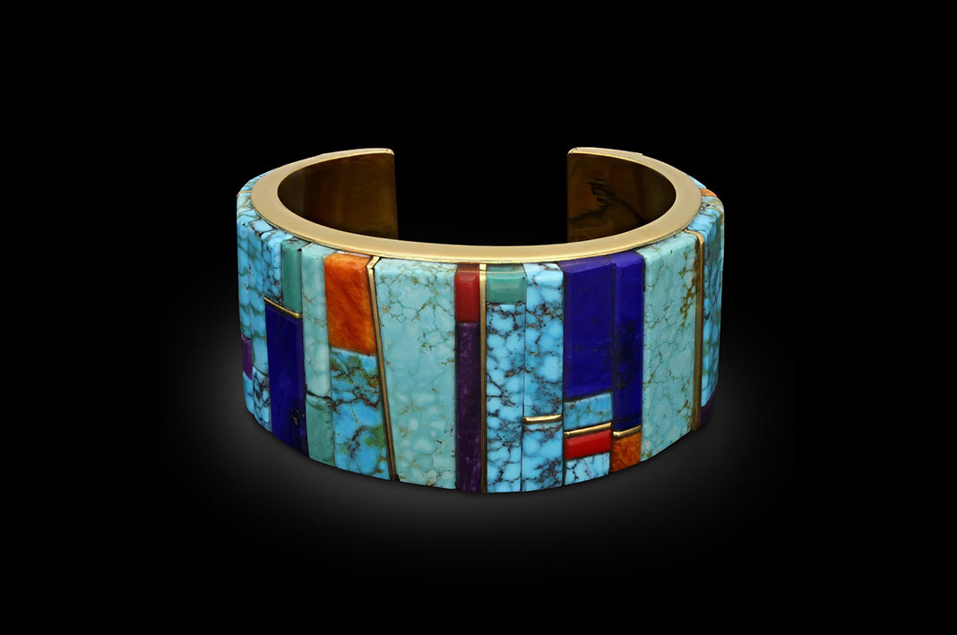 blt130085_5_.HOME Il bracciale rigido in oro giallo 18ct realizzato da Sonwai per Hancocks London. Un intarsio policromo unisce turchese, lapislazzuli, sugilite, conchiglia spiny oyster e rosarita